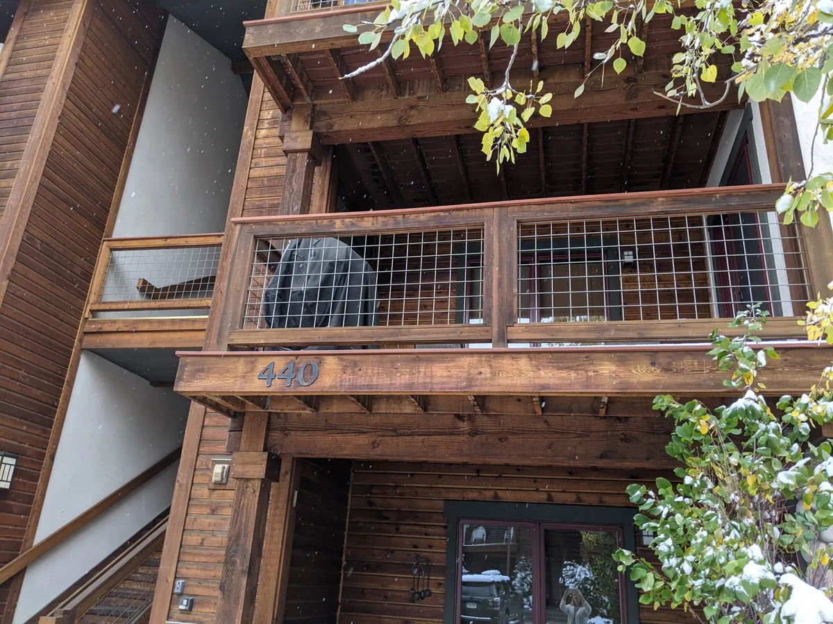 This image shows a welcoming wooden balcony surrounded by snow, with house number 440 visible and green foliage peeking through. The balcony provides a comfortable spot to enjoy the outdoors in any season, whether it's watching falling snow or entertaining guests.