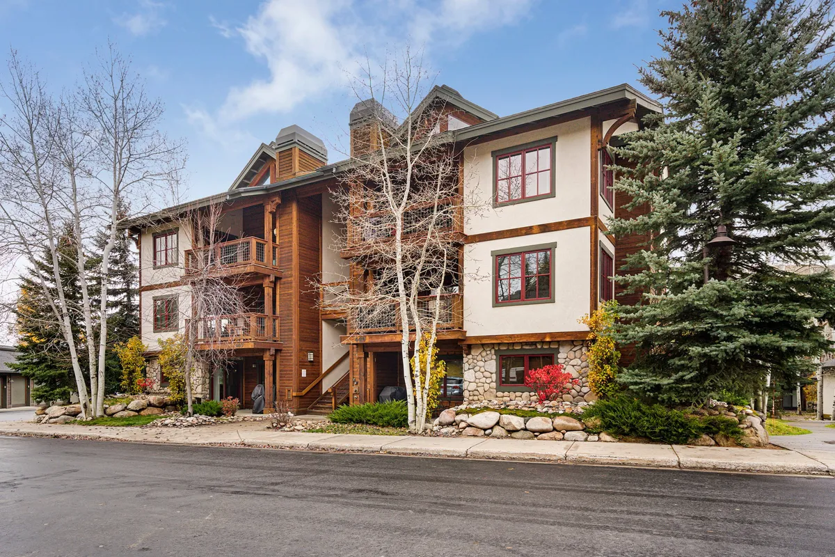 The image reveals a welcoming front porch with a wooden structure, stone landscaping, large windows, and surrounding trees. The entryway is visible, suggesting a transition from outside to inside, and the porch hints at the home’s inviting spirit.