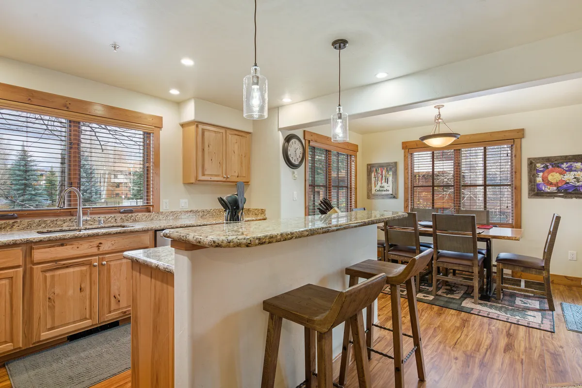 This image features an inviting and warm dining area with a granite countertop, wooden cabinetry, and large windows that fill the space with natural light. The dining table is perfect for working remotely or enjoying shared meals, while the spacious kitchen supports everything from everyday living to entertaining guests.