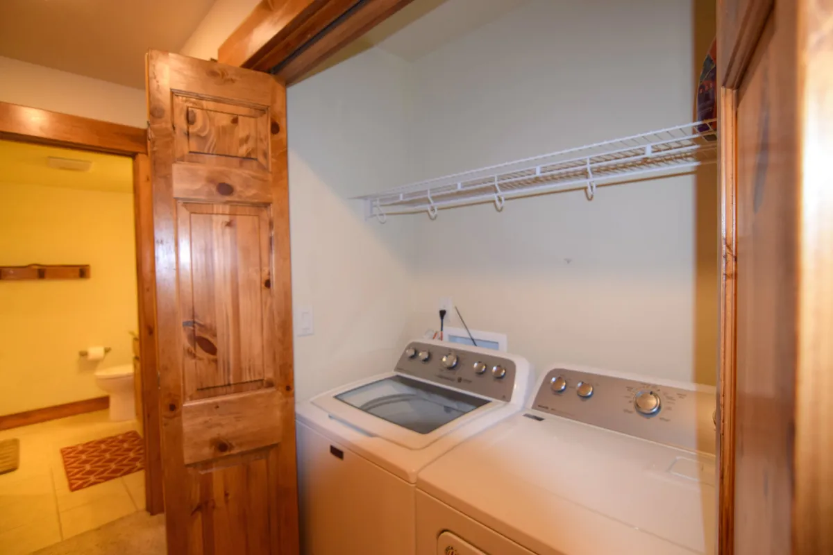 This image shows a practical laundry area with a washing machine, dryer, and a shelf above for organizing supplies. The space exudes efficiency and functionality, with the appliances and built-in shelving suggesting thoughtful design for active lifestyles.