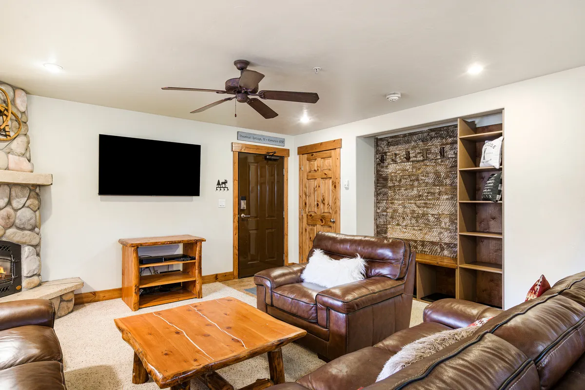 A welcoming living area featuring a stone fireplace, leather sofas, a wooden coffee table, and a TV, radiating warmth and comfort. The space is perfect for relaxing after a day outdoors, socializing, or enjoying family time, and embodies the condo’s home-like comforts.