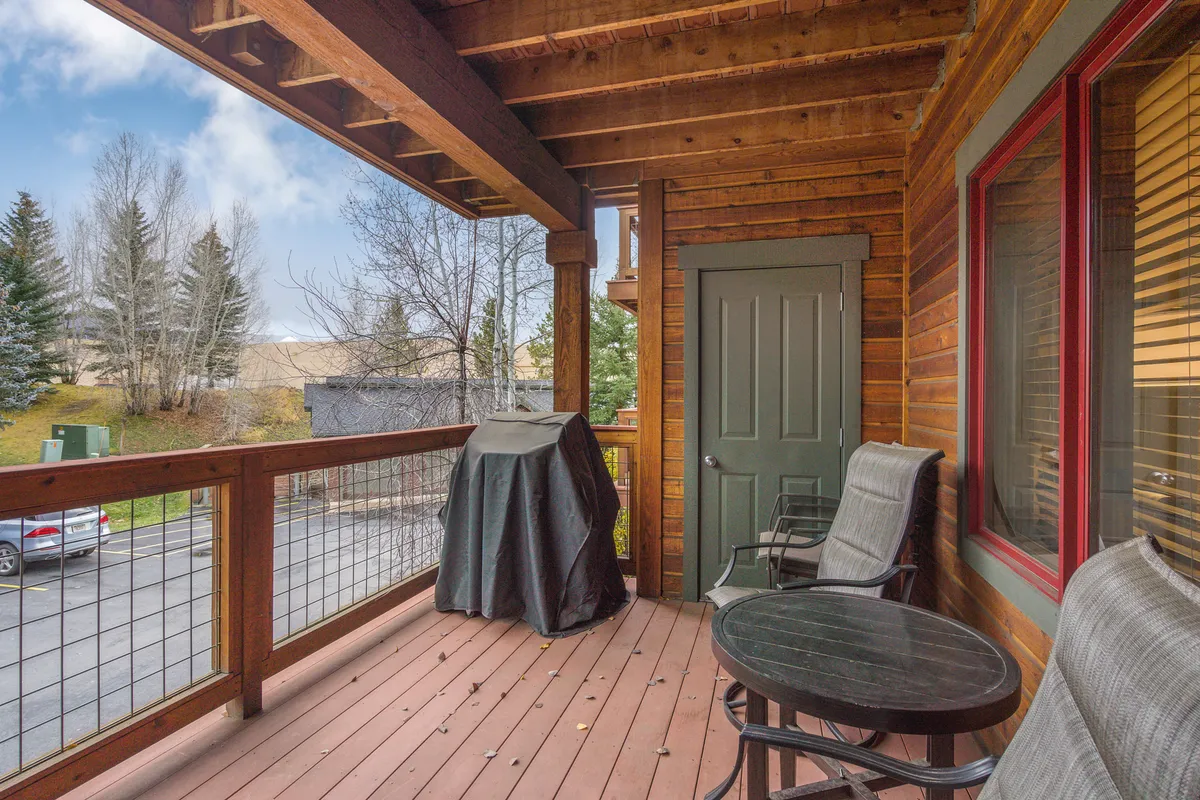An exterior deck view with a covered grill, seating area, and wooden railings, set against a backdrop of trees. While not directly showing snow, the space highlights outdoor living and relaxation opportunities, suggesting a place to unwind after skiing or to prepare for a day on the slopes.