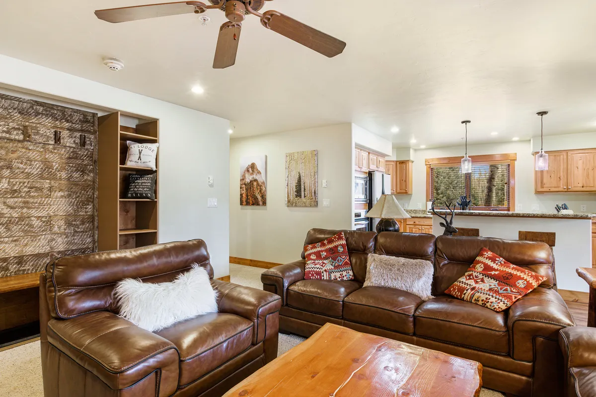 A welcoming living area featuring plush leather sofas, a wooden coffee table, decorative pillows, and artwork on the walls. The space exudes warmth and comfort, inviting guests to relax, socialize, or gather around the fireplace after a day of outdoor adventure.