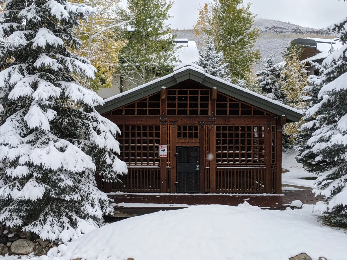 A snowy exterior shot showing the building nestled among frosted trees, with a wooden structure that exudes mountain charm. The tranquil atmosphere hints at the peacefulness guests experience after a fun-filled day on the slopes. The visible snow cover and surrounding nature reinforce the connection to Steamboat's famous winter recreation.
